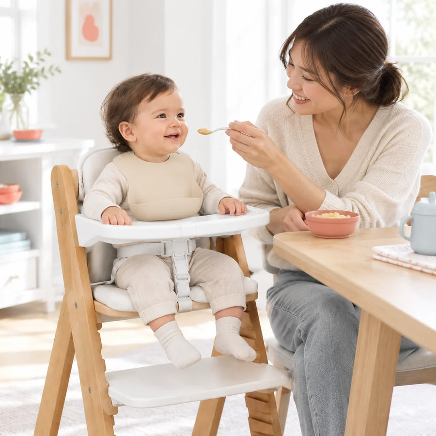A parent supervising their baby's mealtime in a wooden high chair